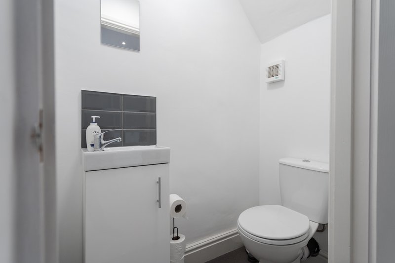 Small bathroom with white sink vanity, toilet, and dark tile backsplash