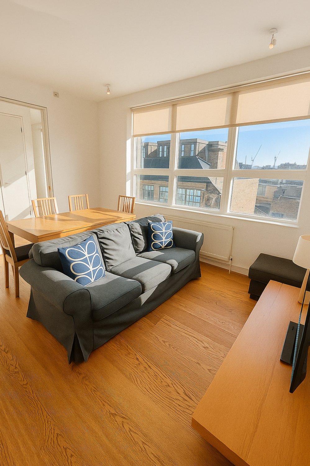 Bright living room with grey sofa, wooden dining table, hardwood floor and city views