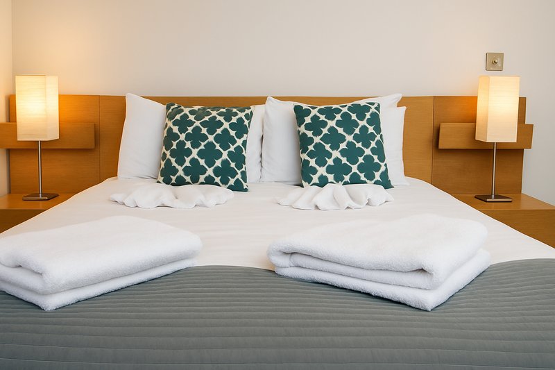 Modern bedroom with double bed, white pillows, patterned cushions, and bedside lamps