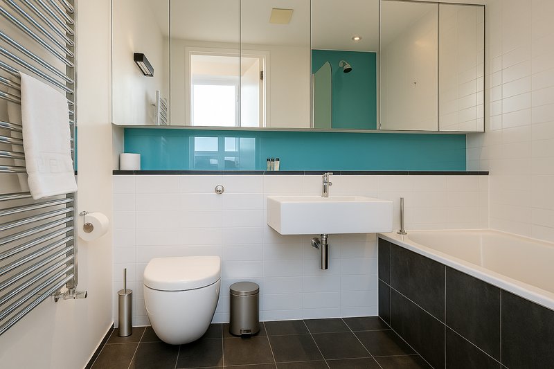 Modern bathroom with white toilet, wall-mounted sink, large mirror, teal backsplash and dark floor tiles