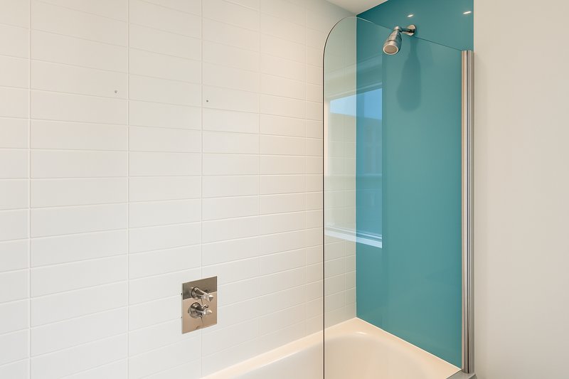 Modern bathroom with walk-in shower, white tile walls, turquoise glass panel and chrome fixtures