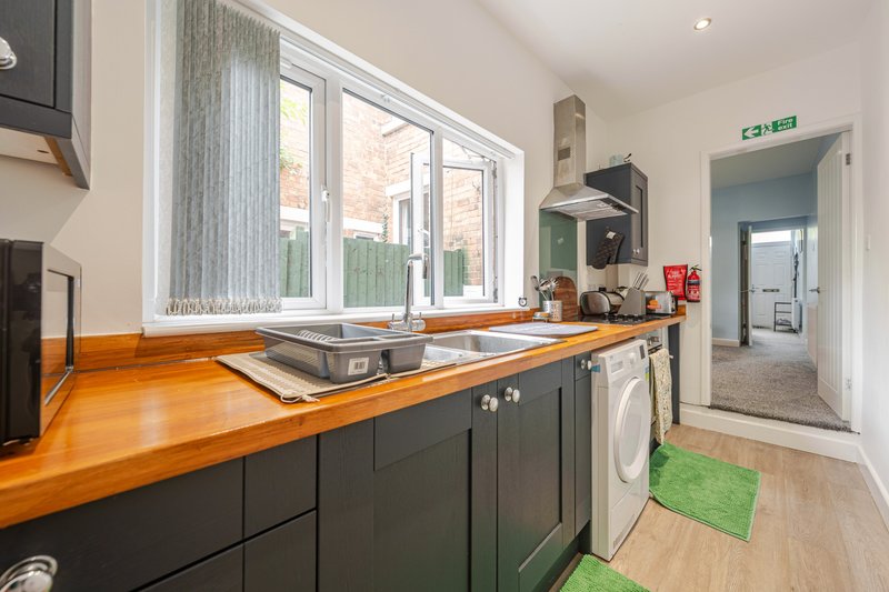 Modern kitchen with dark cabinetry, wooden countertop, integrated appliances and large window