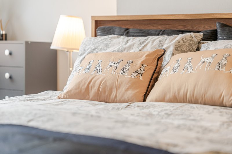 Modern bedroom with wooden bed frame, decorative pillows, white bedding and bedside lamp