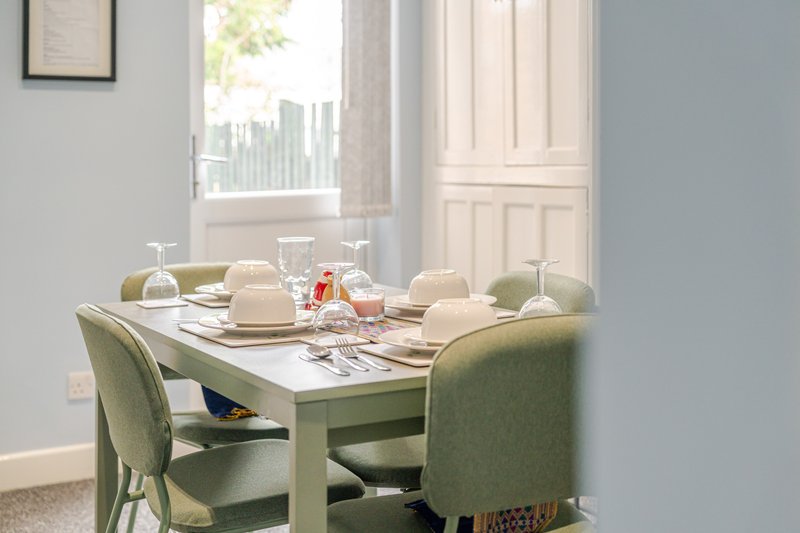 Dining table with green chairs, place settings, and window with city view