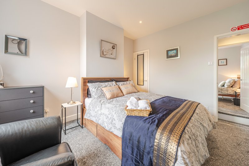 Bedroom with wooden bed frame, blue bedding, side table lamp, and doorway to ensuite