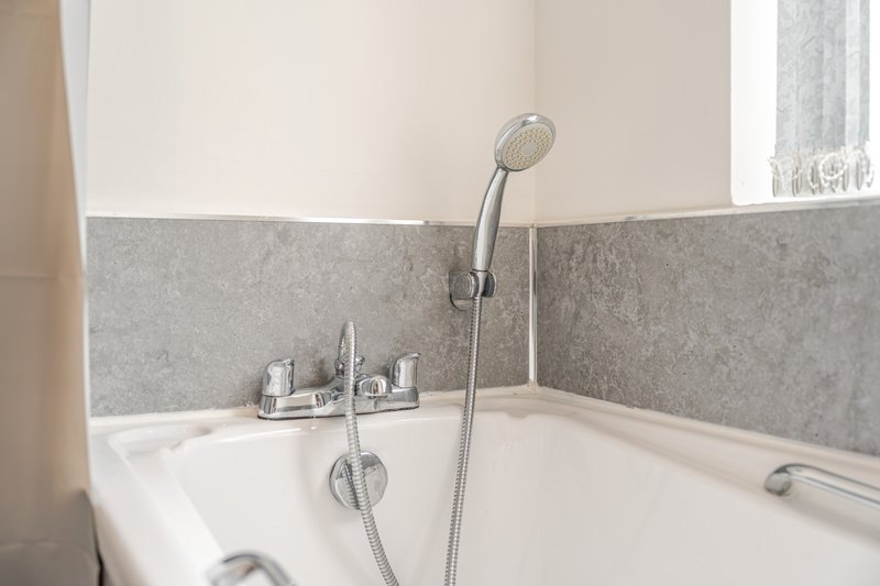 Modern bathroom with white bathtub, gray tile surround, and handheld shower head
