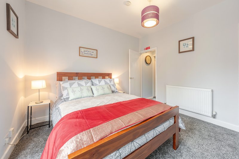 Bright bedroom with double bed, red throw, wooden headboard, bedside lamp and ceiling light fixture