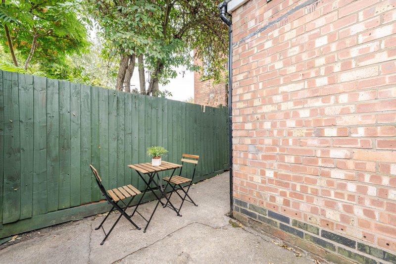 Outdoor patio area with green fence, brick wall, small table and chairs