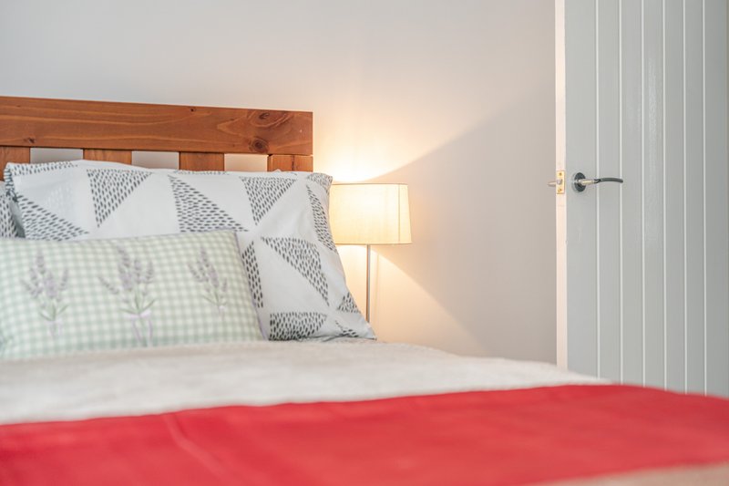 Bedroom with wooden headboard, patterned pillows, red blanket and bedside lamp