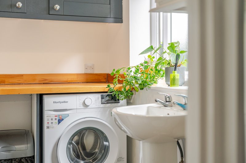 Utility room with washing machine, wall-mounted sink, window, and potted plant