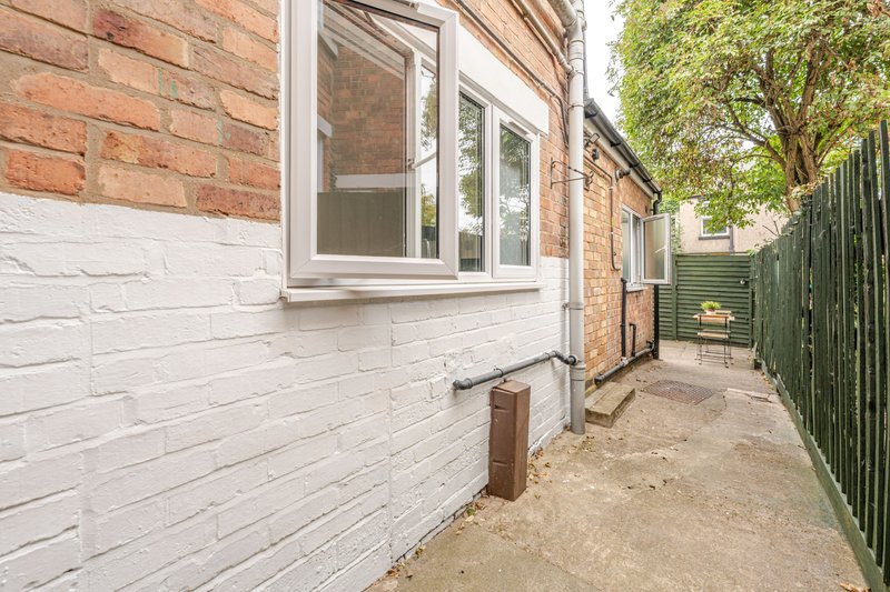 Brick and white-painted house exterior with windows, side pathway, and green fence