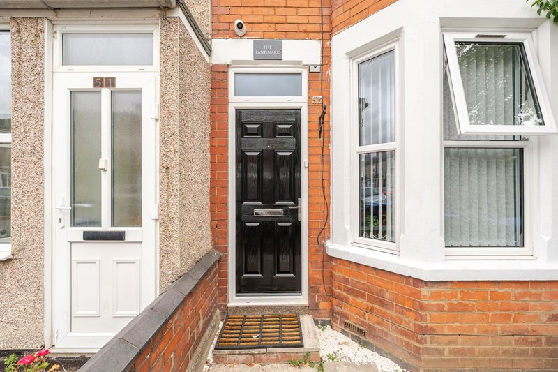 Brick terraced house exterior with white and black front doors, windows, and entrance doormat