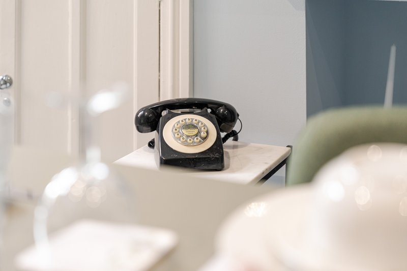 Vintage black rotary telephone on white shelf with blurred foreground and neutral background