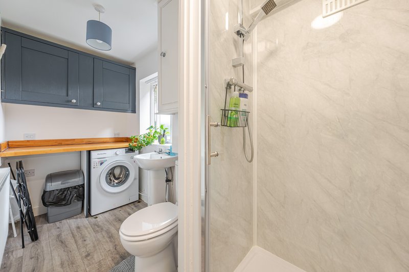 Modern bathroom with toilet, shower enclosure, washing machine and blue cabinetry