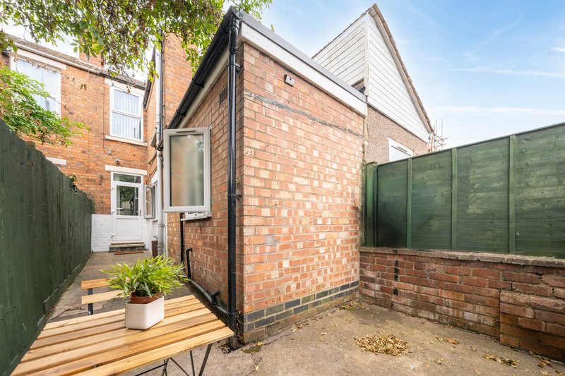Brick extension with wooden deck, potted plant, green fence and patio area