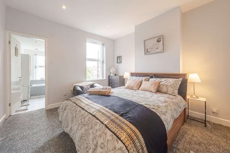 Bright bedroom with double bed, patterned bedding, wooden headboard, and access to ensuite bathroom