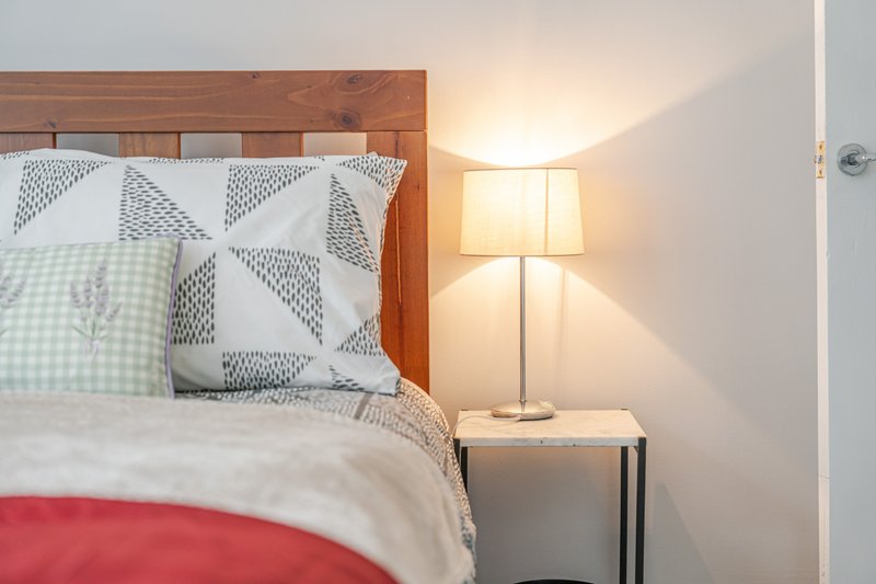 Bedroom with wooden bed frame, patterned pillows, bedside lamp and nightstand