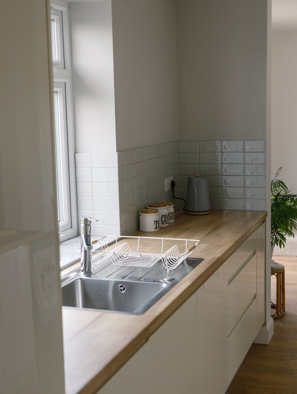 Modern kitchen sink with wooden countertop, white cabinetry, and tiled backsplash