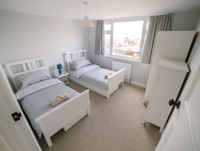 Bright bedroom with two single beds, white furniture, striped bedding and window view