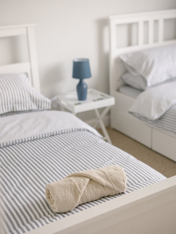 Twin bedroom with striped bedding, white headboards, bedside table and lamp