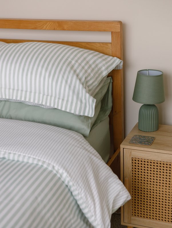 Wooden bed frame with striped bedding, green throw pillow, and bedside table lamp