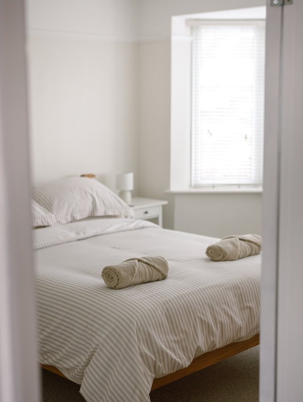 Small bedroom with single bed, striped bedding, white pillows, wooden frame and window