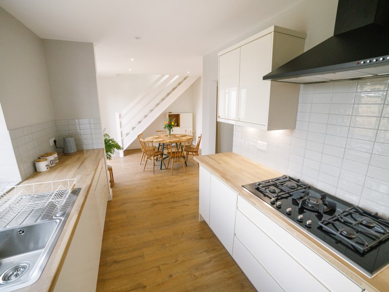 Modern kitchen with white cabinetry, wooden countertops, gas hob and dining area beyond