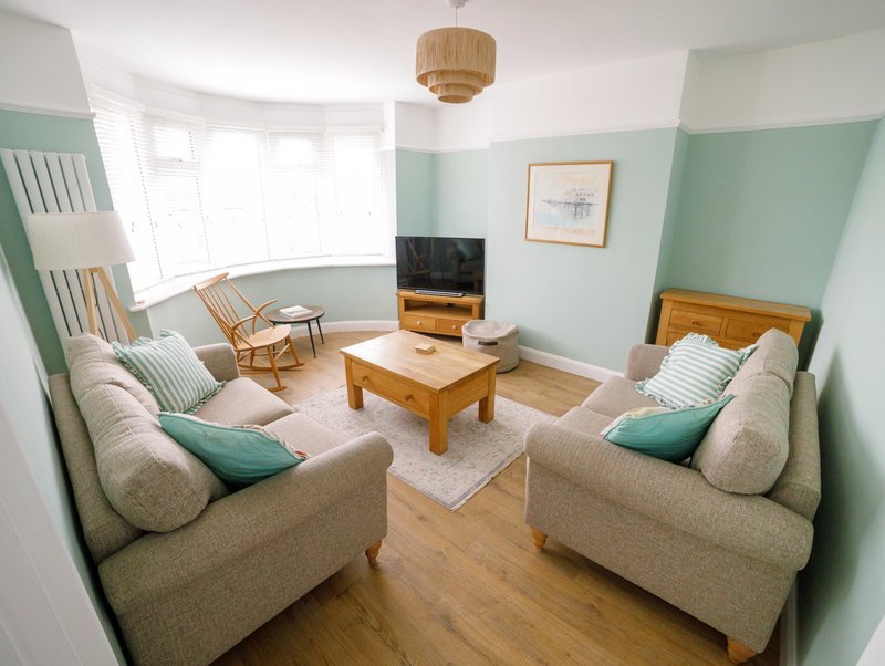 Modern living room with two beige sofas, wooden coffee table, TV unit, and bay window