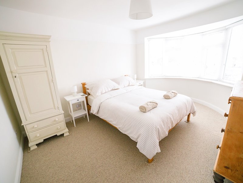 Bright bedroom with king double bed, white bedding, wooden furniture and large window