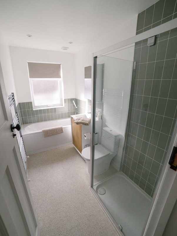 Modern bathroom with shower enclosure, bathtub, window, and green tile walls