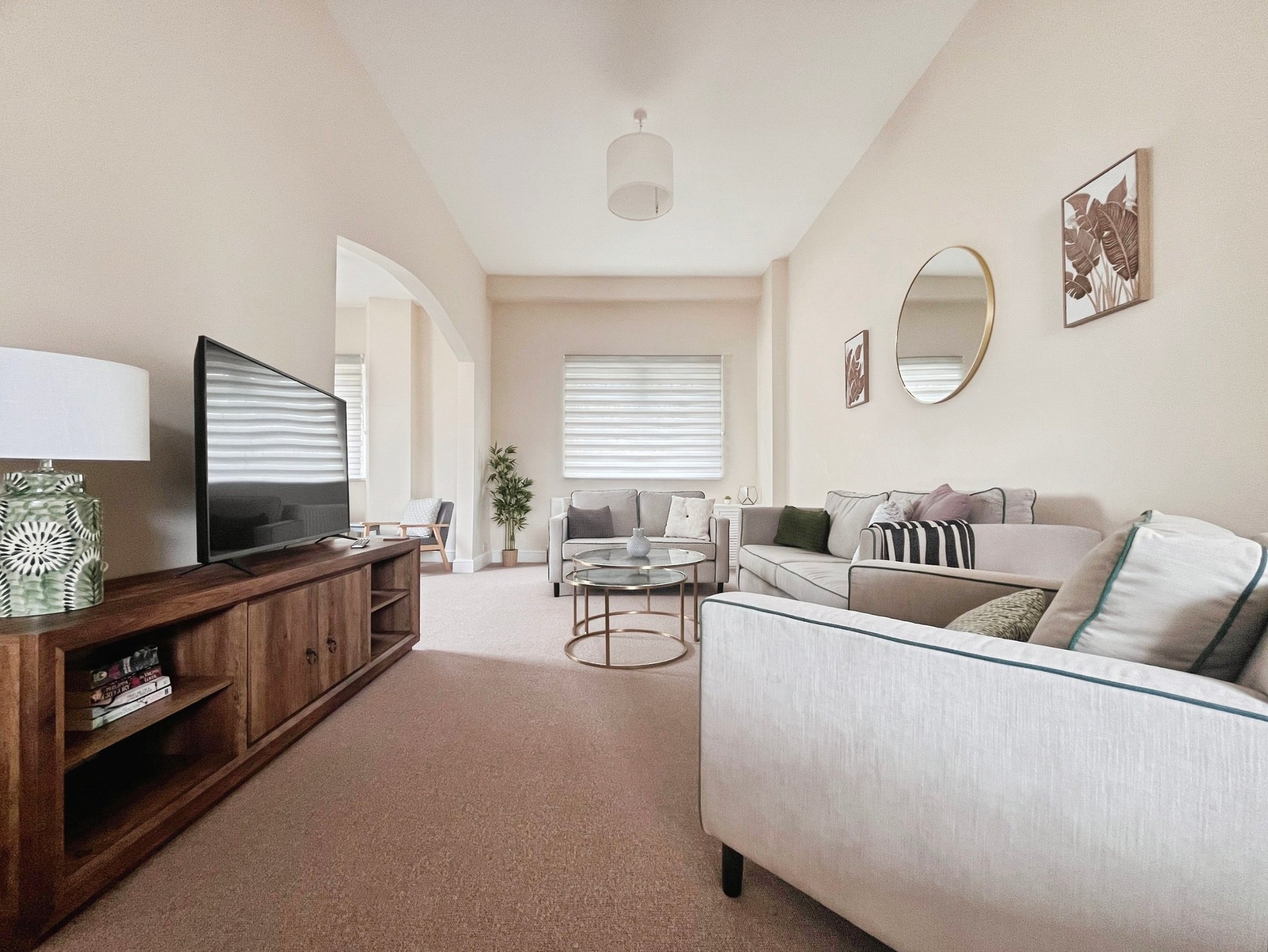 Spacious living room with cream sofa, wooden TV stand, and neutral décor throughout