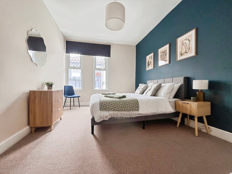 Modern bedroom with double bed, teal accent wall, wooden furniture, and large windows