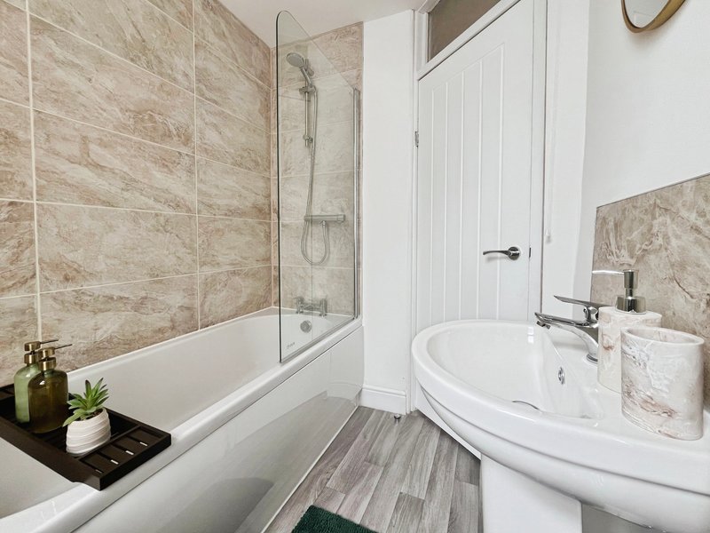 Modern bathroom with corner bathtub, glass shower screen, pedestal sink and marble-effect tiling