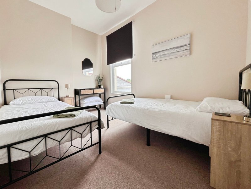 Bright twin bedroom with two metal-frame beds, wooden dresser, window with black blind