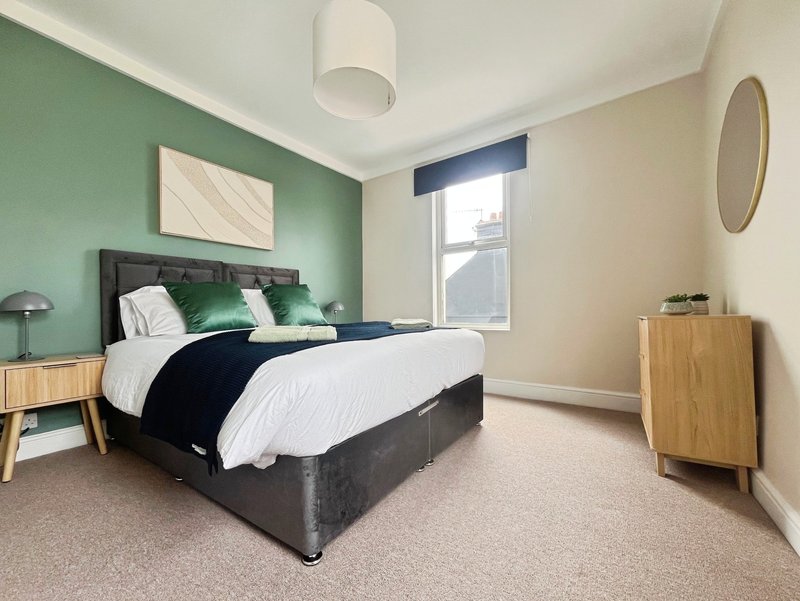 Modern bedroom with double bed, green accent wall, wooden furniture and large window