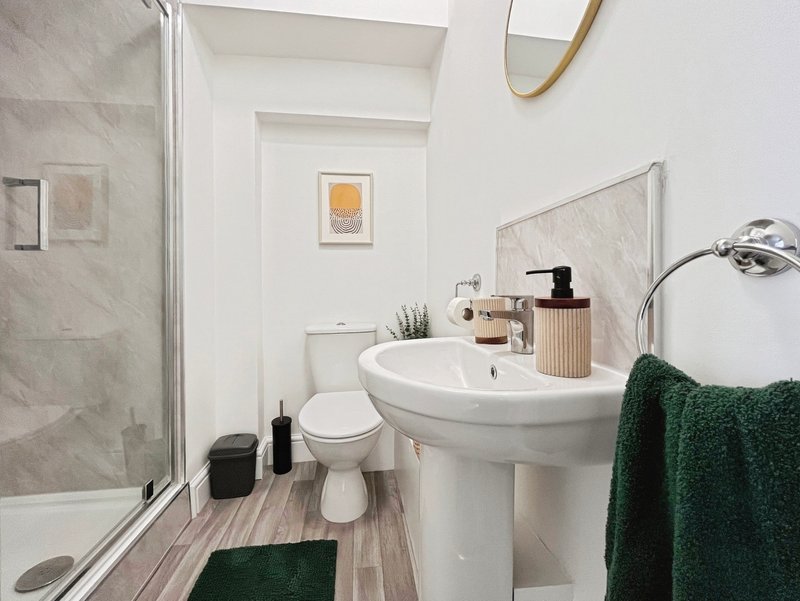 Modern bathroom with pedestal sink, toilet, shower cubicle, green towels and white walls