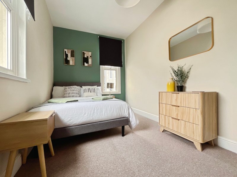 Modern bedroom with double bed, wooden furniture, green accent wall and natural light from window