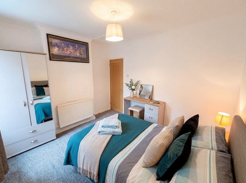 Bright bedroom with double bed, white wardrobe, wooden dresser, and pendant ceiling light