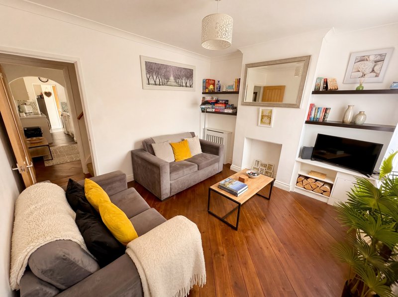 Bright living room with two sofas, wooden floor, shelving, TV, and decorative cushions