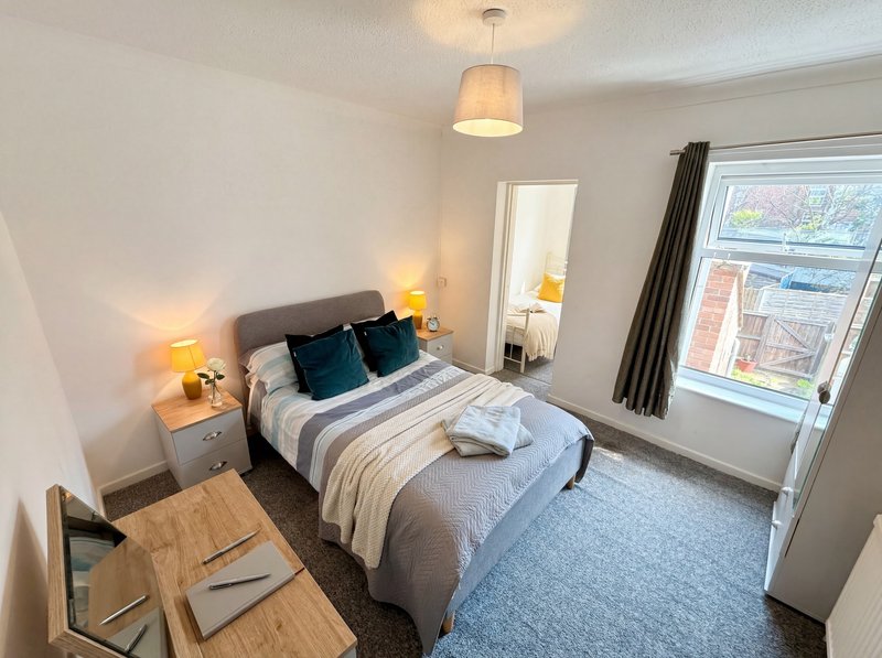 Bright bedroom with double bed, bedside tables, desk, mirror, window with curtains and pendant light