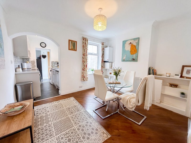 Open-plan living and kitchen space with wooden floors, dining table, chairs, and shelving