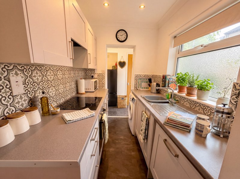Modern galley kitchen with white cabinets, patterned backtile, and potted plants on windowsill