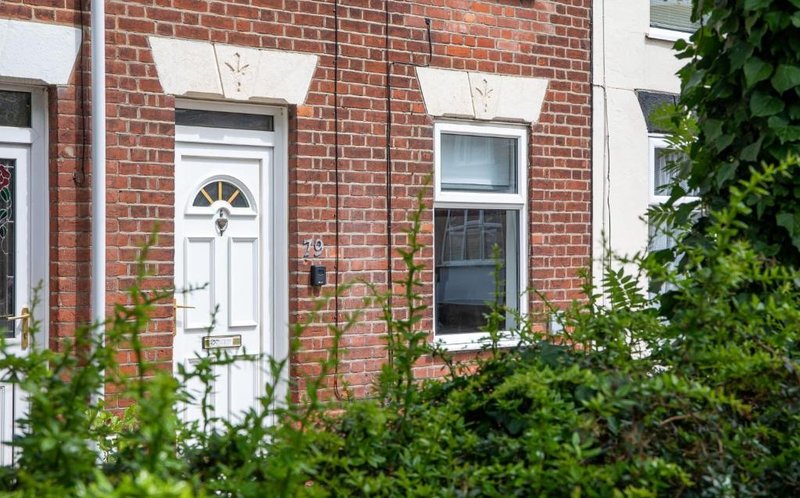 Red brick Victorian terraced house with white door, sash windows and climbing ivy