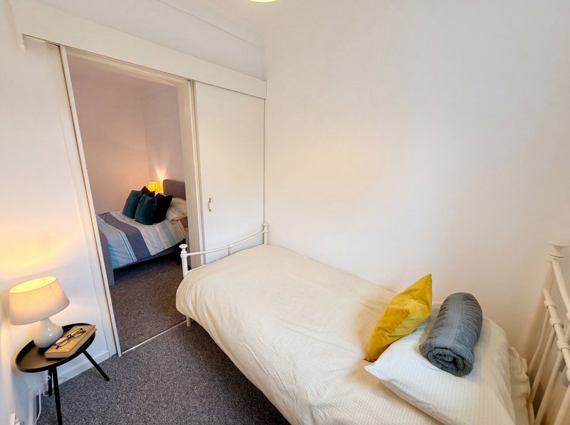 Compact bedroom with single bed, yellow cushion, lamp, and mirrored wardrobe door