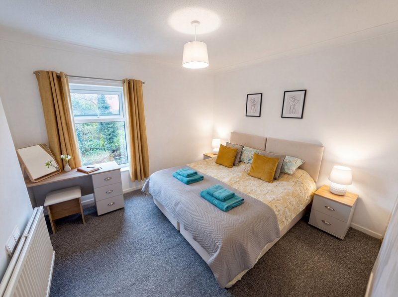 Bright bedroom with double bed, desk, window with gold curtains and bedside lamps