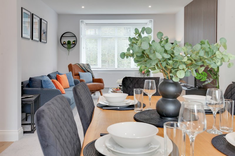 Open-plan living and dining area with set table, sofa, armchair and potted plants by window