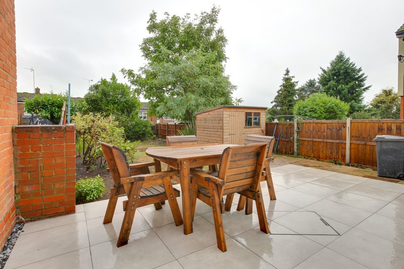 Paved garden patio with wooden dining table, chairs, brick walls and mature trees
