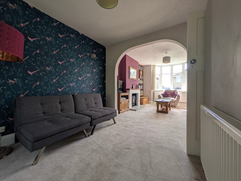 Open-plan living space with dark patterned feature wall, grey sofa, and view through archway to bedroom seating area