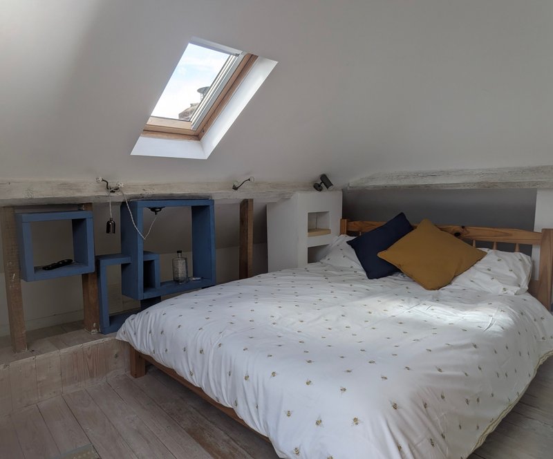 Attic bedroom with skylight, double bed, blue storage unit and wooden beams