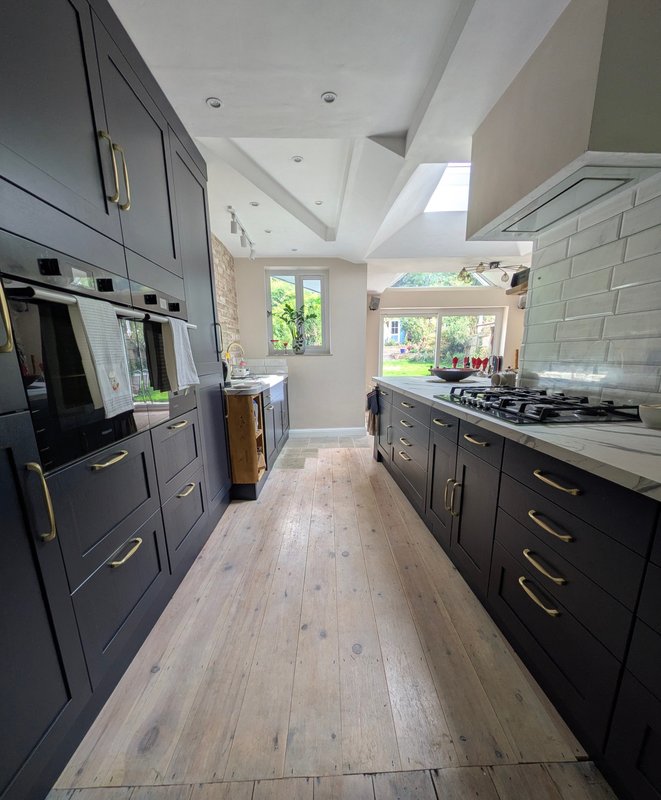 Modern kitchen with dark cabinetry, stainless steel appliances, wooden flooring and bright windows